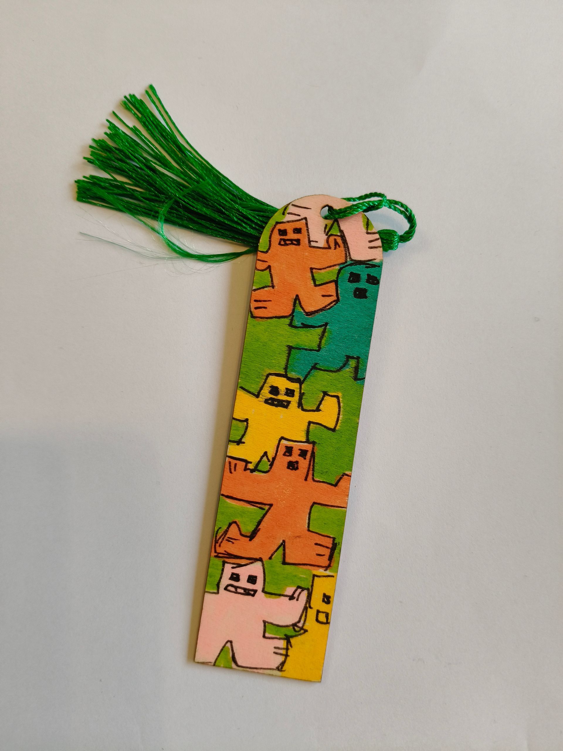 Een handgemaakte boekenlegger versierd met kleurrijke, cartoonachtige monsterfiguurtjes en een groene kwast aan de bovenkant.