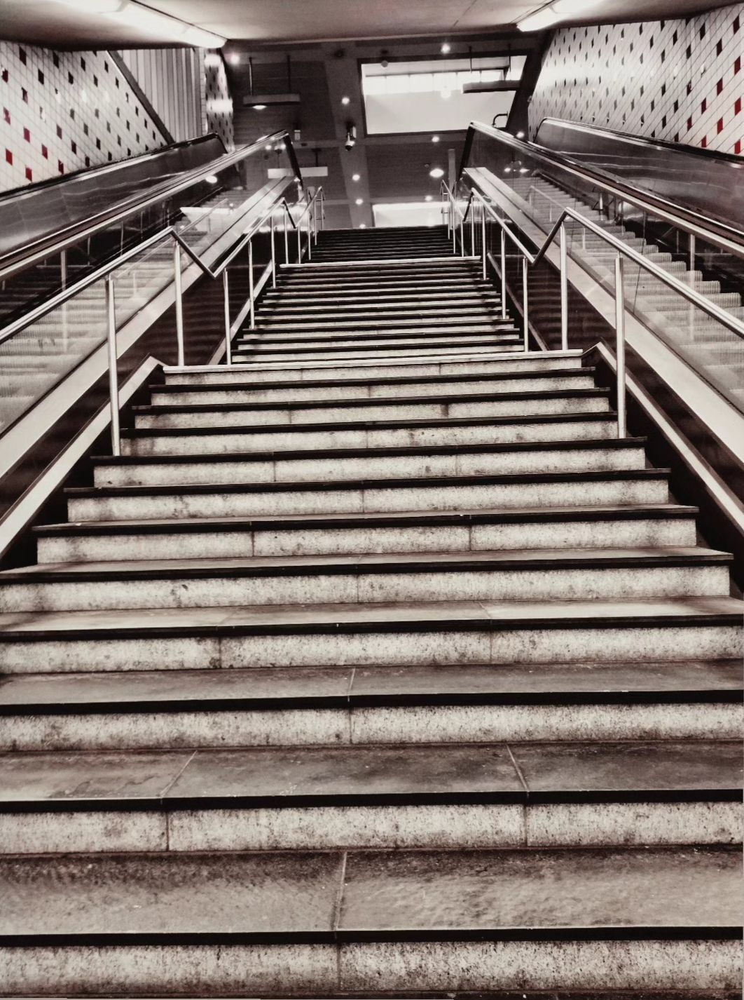 Een lange, steile binnentrap met stenen treden en metalen leuningen leidt omhoog naar een licht platform.