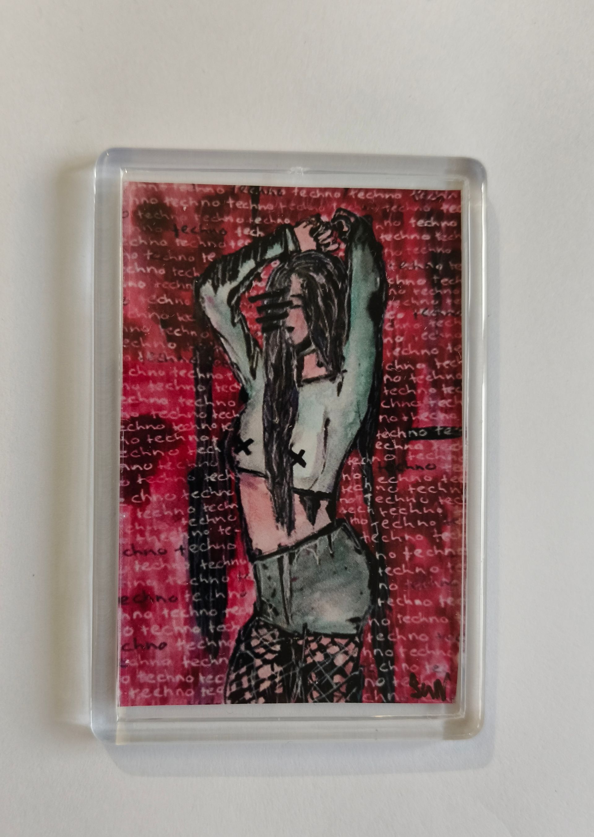 Een rechthoekige acrylmagneet met een afbeelding van een figuur met lang haar tegen een achtergrond van rode tekst.