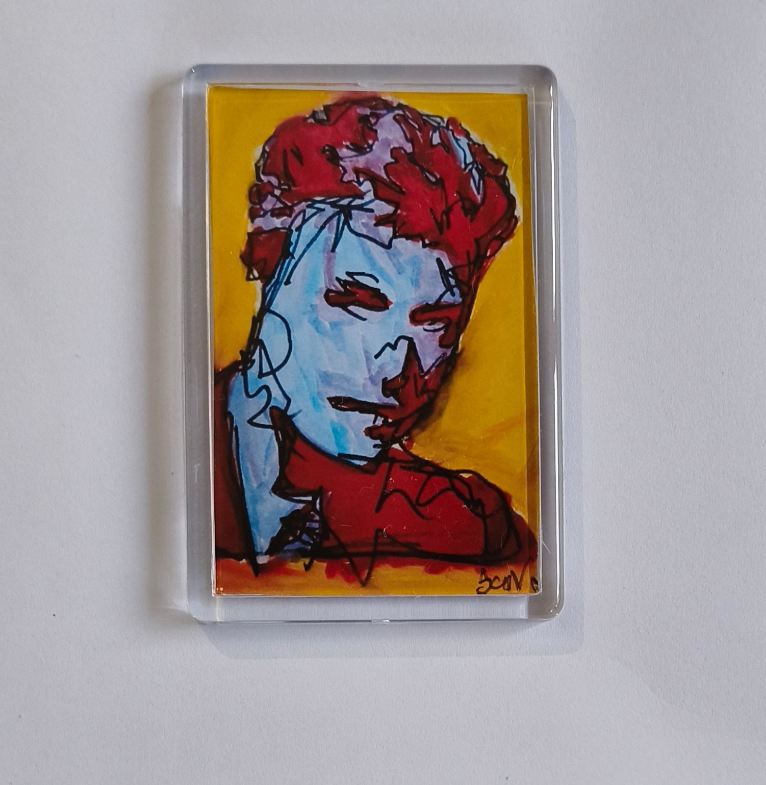 koelkast magneet van een gestileerd van David Bowie met een blauw gezicht en rood haar, tegen een felgele achtergrond.