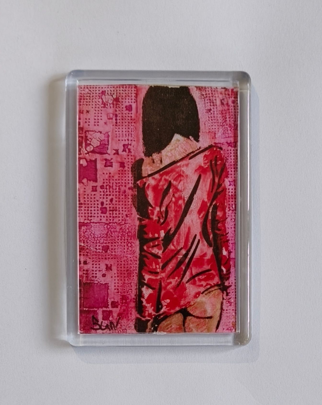Een koelkast magneet van kunstwerk met een persoon in een rood shirt tegen een roze achtergrond met textuur en patroon.