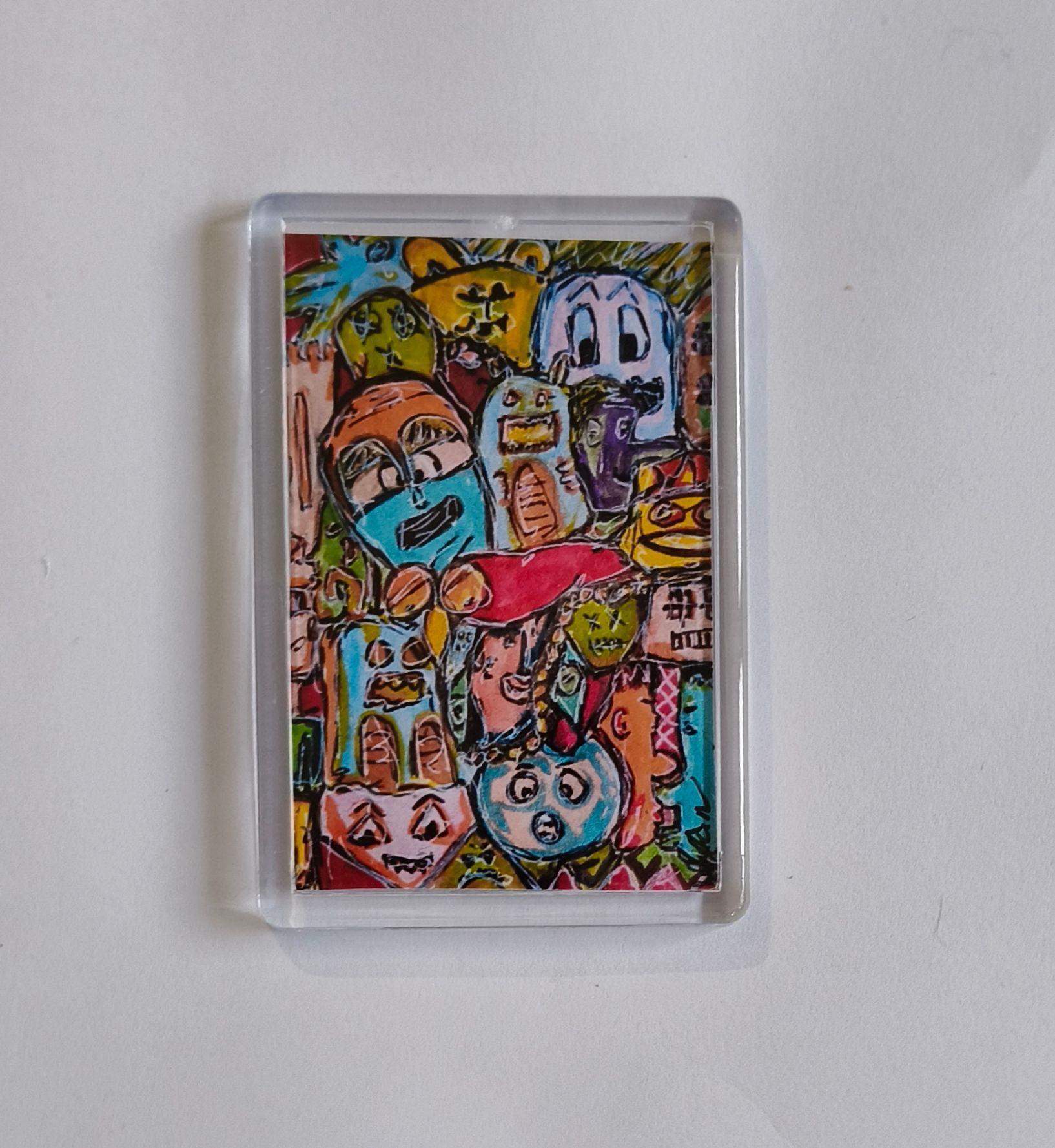 Een koelkast magneet met daarin een levendige, kleurrijke doodle-collage met diverse grappige cartoongezichtjes.