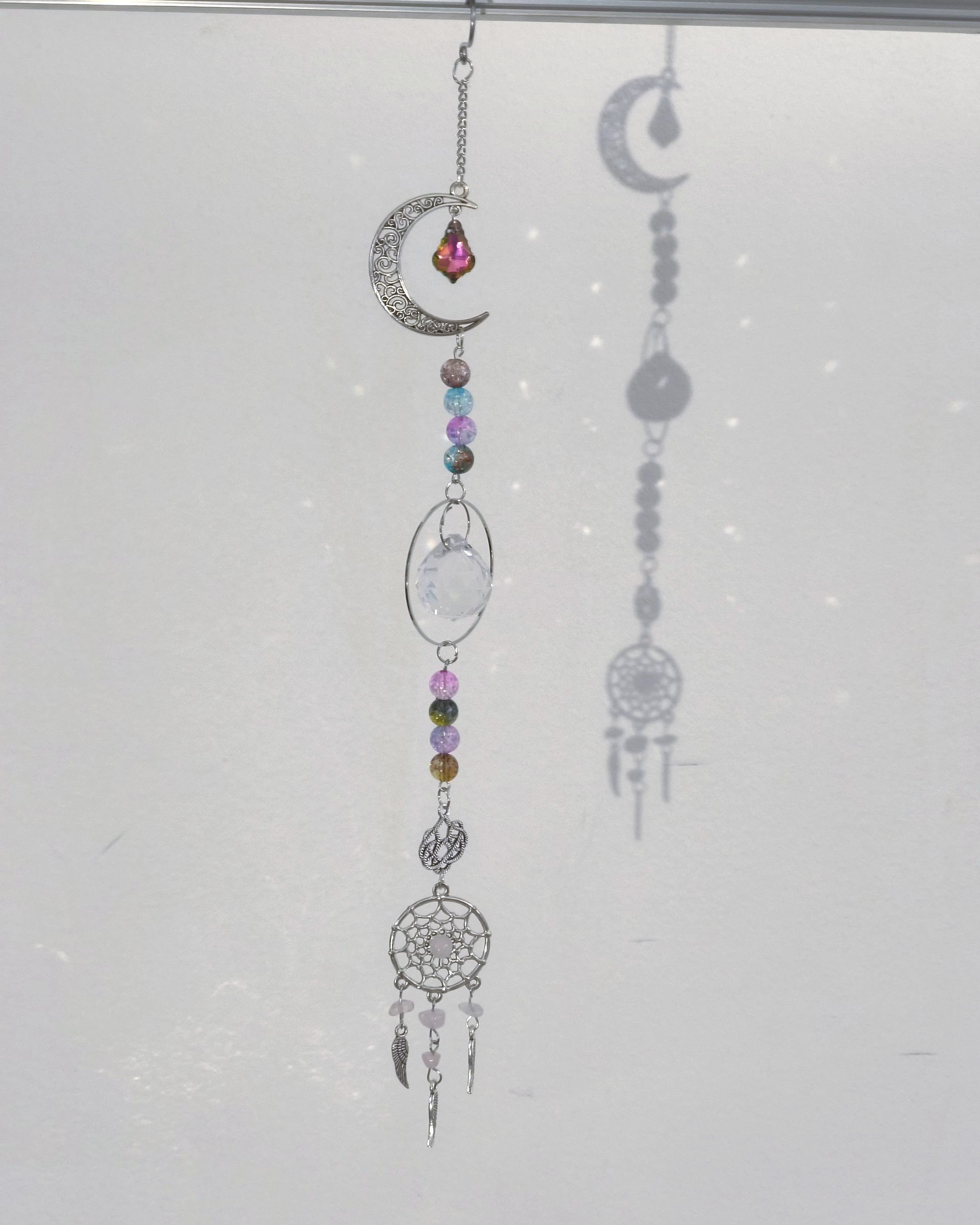 Een hangornament met een halve maan, kleurrijke kralen, een rond frame en een kleine dromenvanger aan de onderkant.