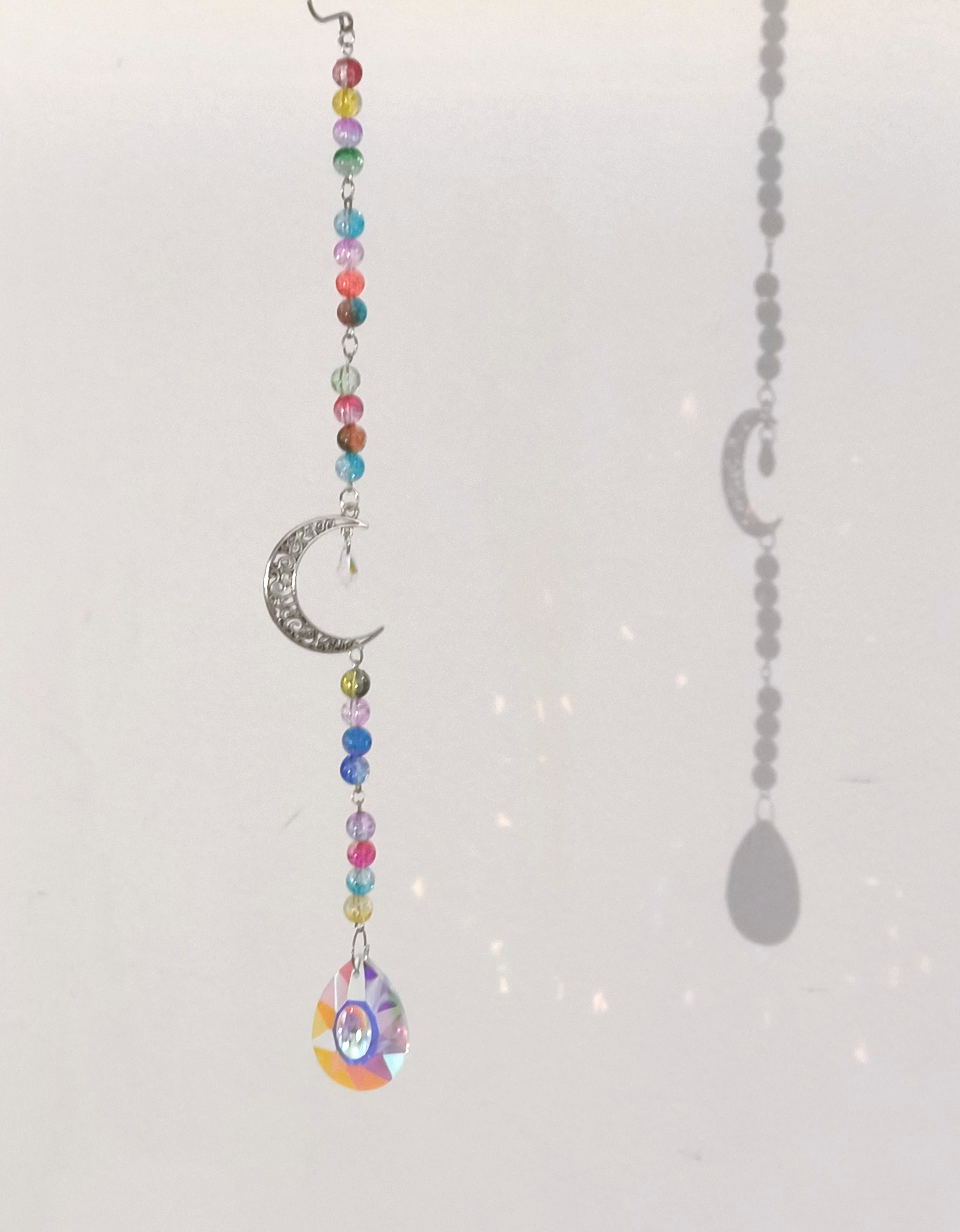 Een met kralen versierde raamhanger met een zilveren halvemaanvormige hanger en een iriserend druppelvormig kristal.