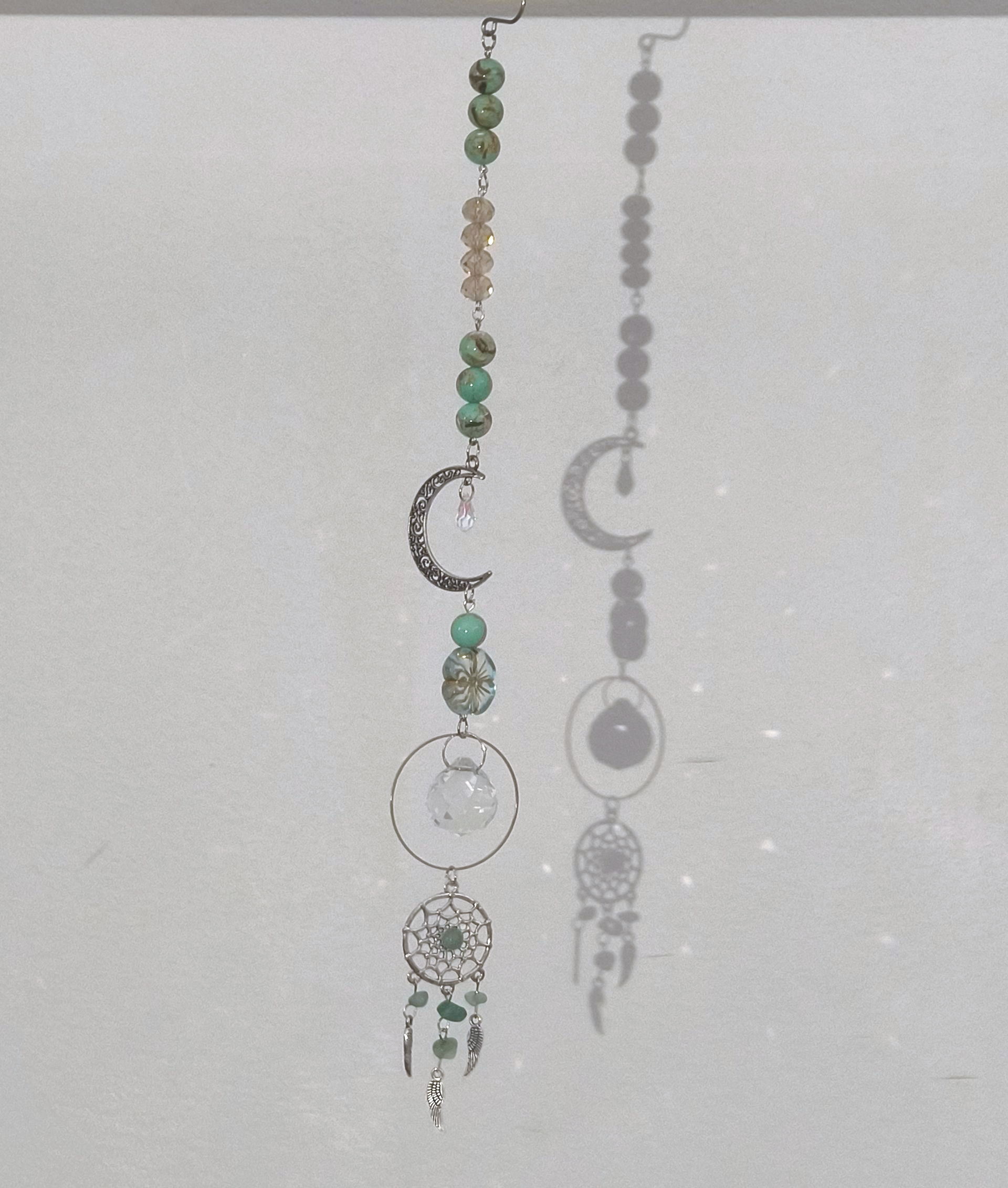 Een decoratief  ornament met groene kralen, een zilveren halve maan, een helder kristal en een klein dromenvangerbedeltje.