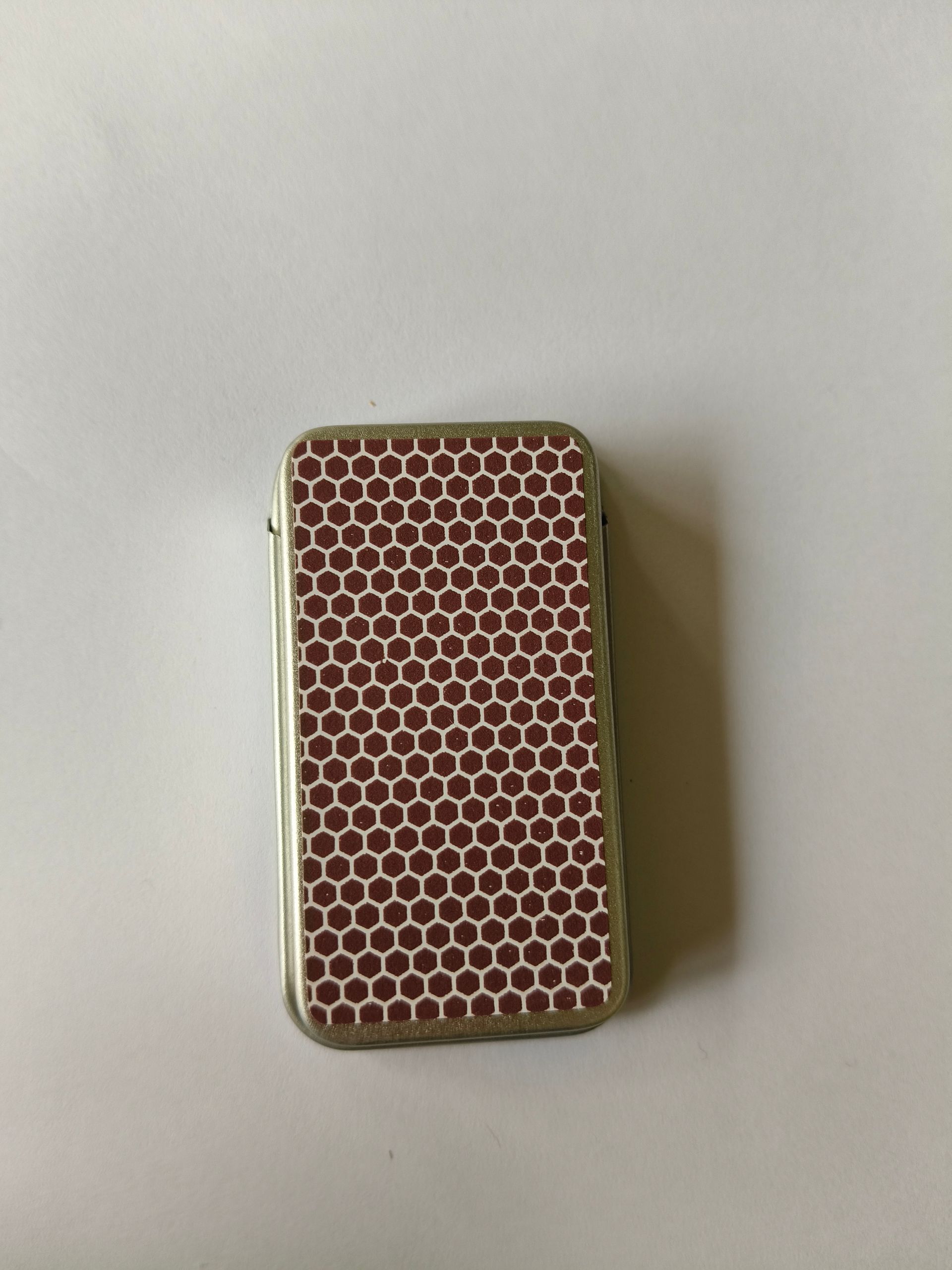 Een metalen blikje met lucifers, met een decoratief zon- en maanmotief op het deksel tegen een witte achtergrond.