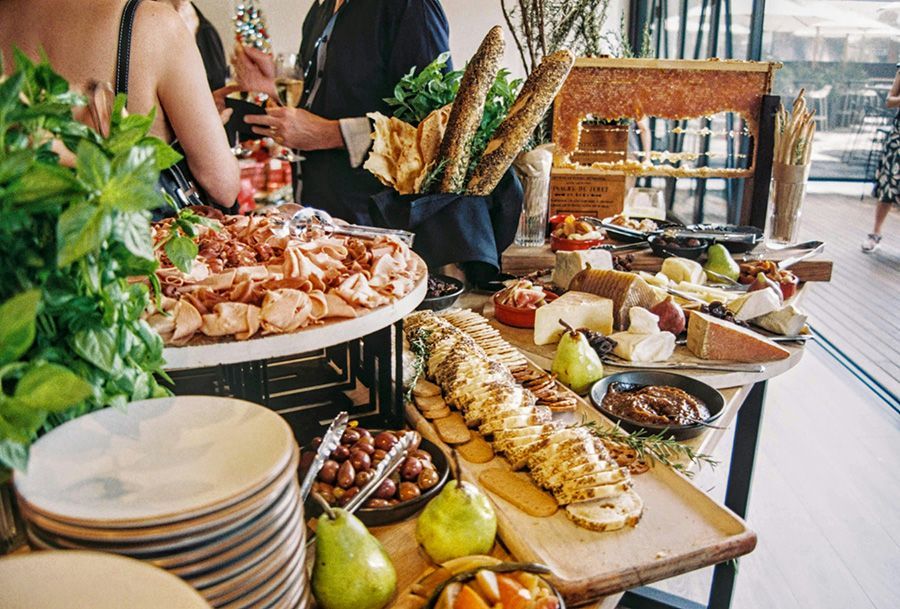 A buffet table laden with meats, cheeses, fruit, and bread; people are gathered around.