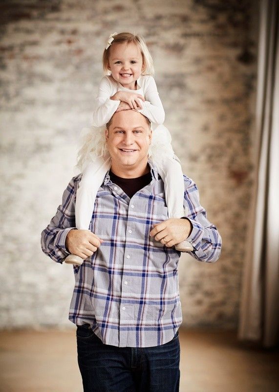 Smiling child sitting on a man's shoulders indoors, both wearing plaid shirts.