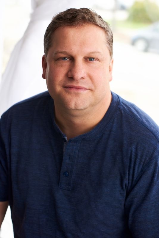 Man in a blue shirt seated indoors, facing the camera with a slight smile.