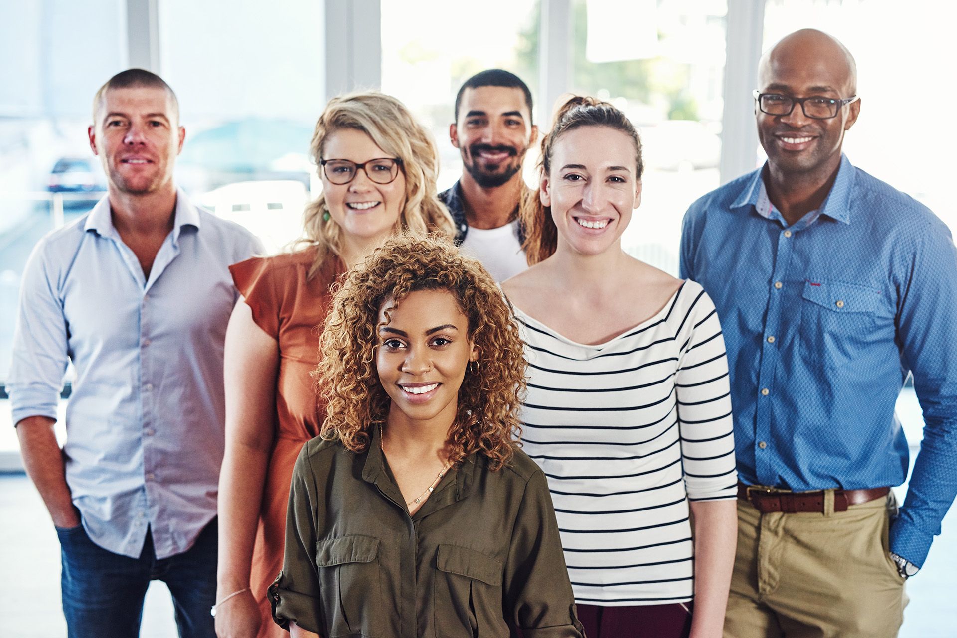 Five smiling coworkers standing together in a bright office lobby
