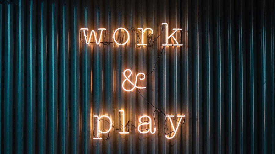 Neon sign reading “work & play” on a dark striped background