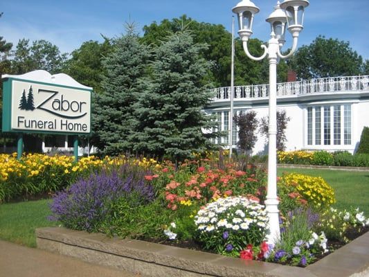 Zabor Funeral Home sign beside landscaped flowers and a white lamp post
