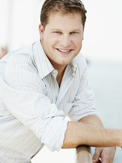 Smiling man in a white striped shirt leaning forward against a bright white background