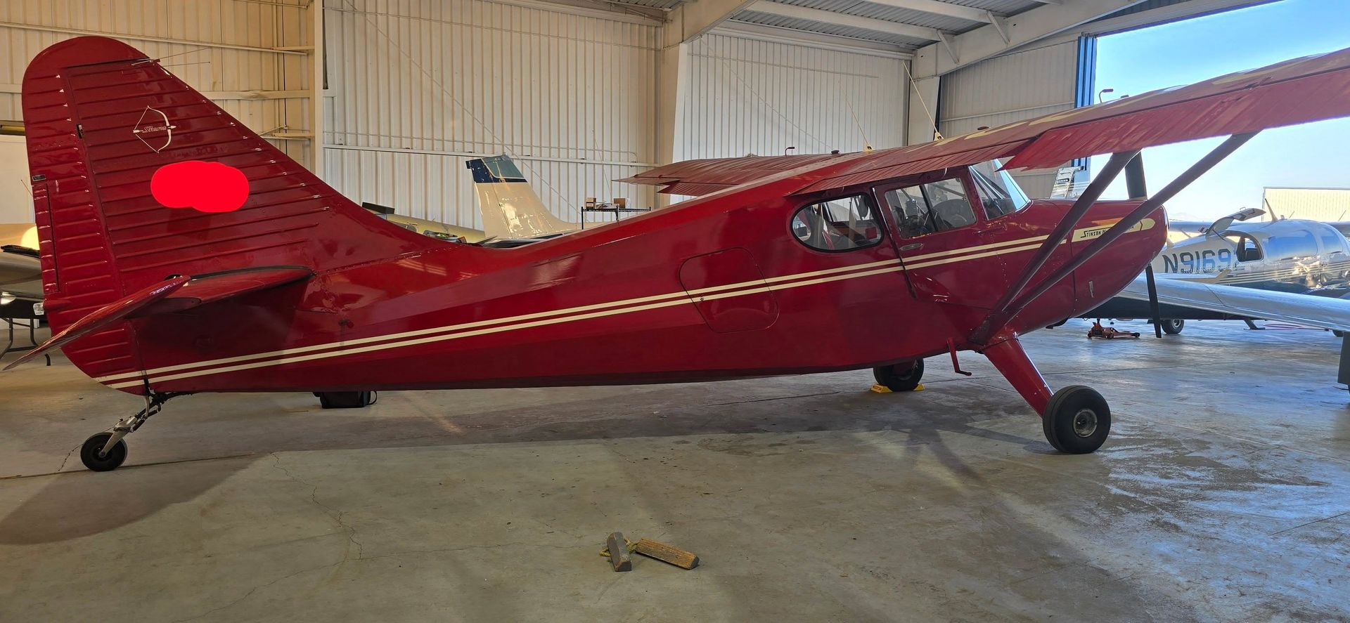 Red vintage single-engine airplane parked inside a hangar.