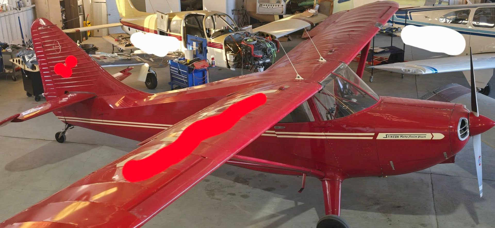 Red model airplane with white stripes displayed indoors in a workshop or hangar.
