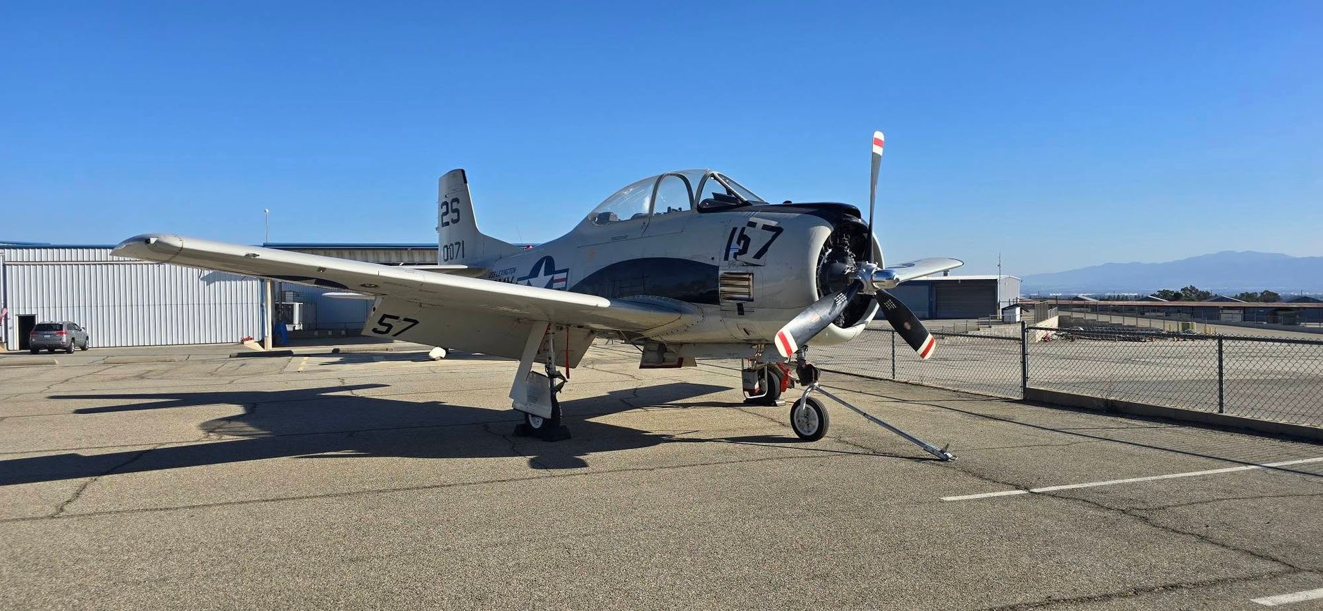 Small silver propeller airplane parked on a runway under a clear sky.