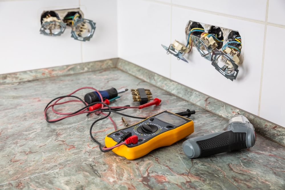 Electrical tools on a countertop beside two exposed wall outlets with loose wiring.