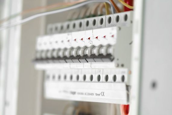 Electrical circuit breaker panel with rows of switches and red wiring inside a white cabinet