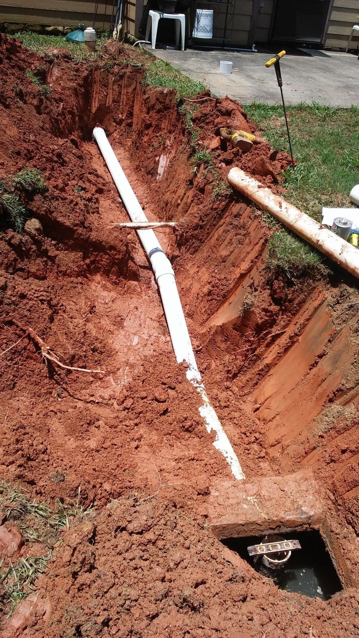Excavated red dirt trench with white PVC pipes and a utility opening at the bottom