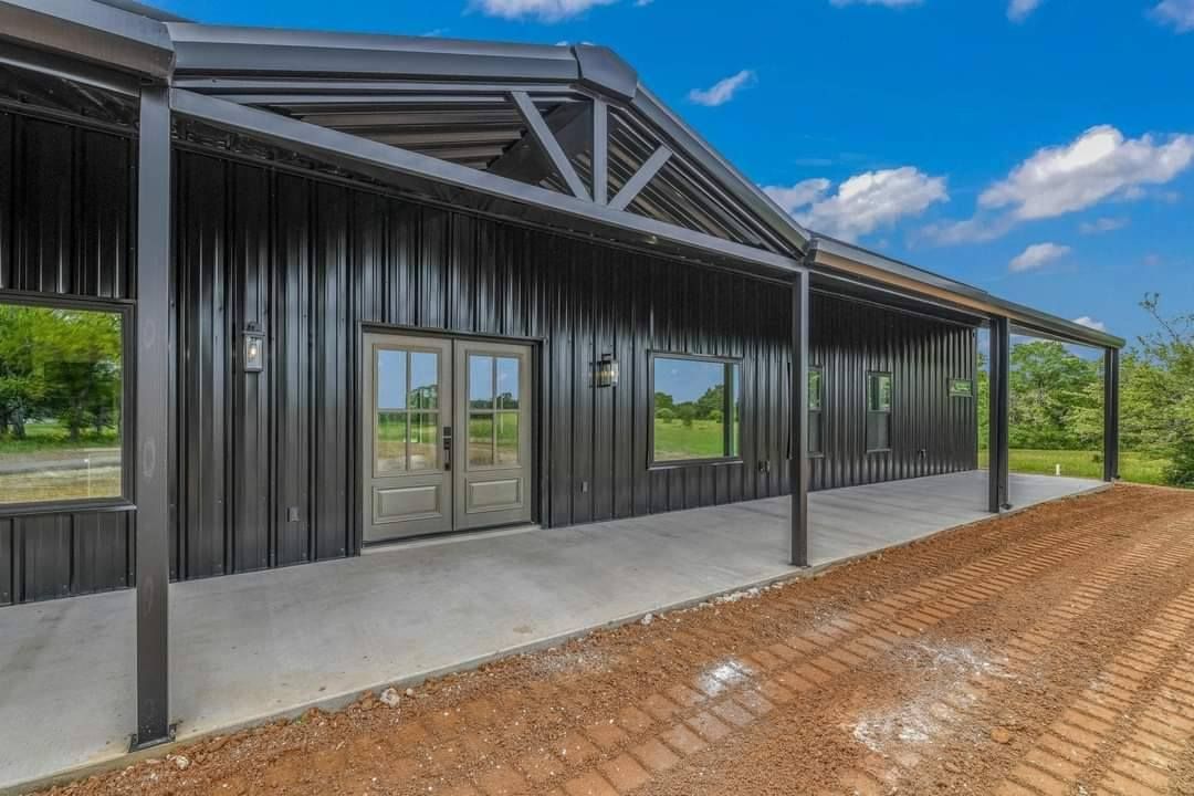 Modern black steel house with covered porch and concrete patio under a blue sky