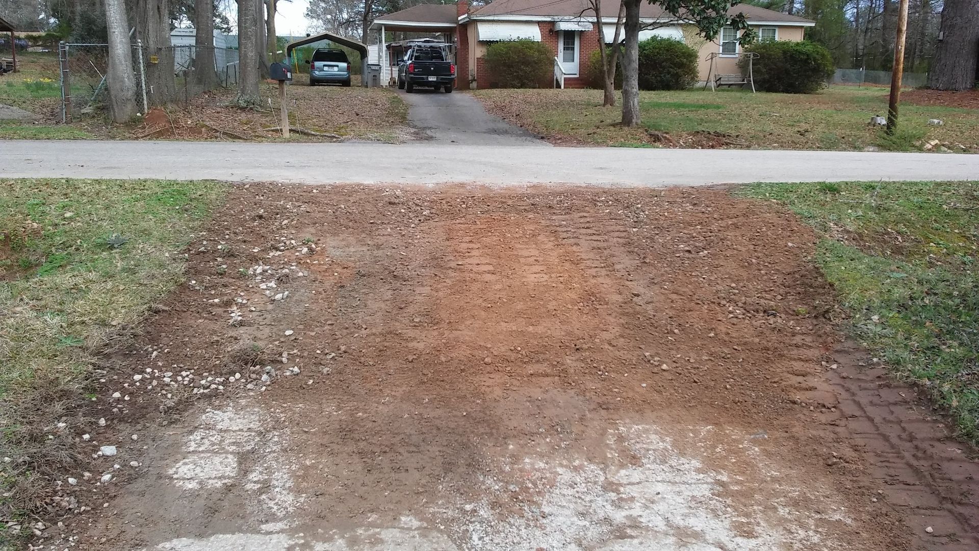 Gravel driveway leading to a suburban street, with a car and houses in the background.