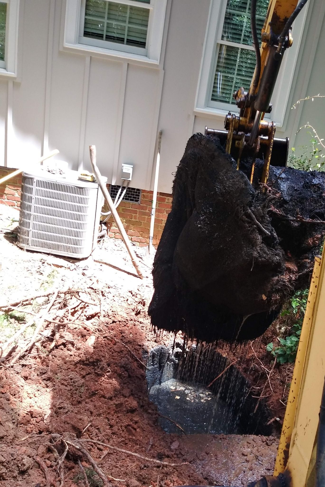 Backyard construction site with excavator digging near a house, pile of dirt in foreground