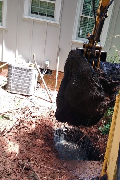 Excavator digging beside a house, moving dirt in a narrow backyard area