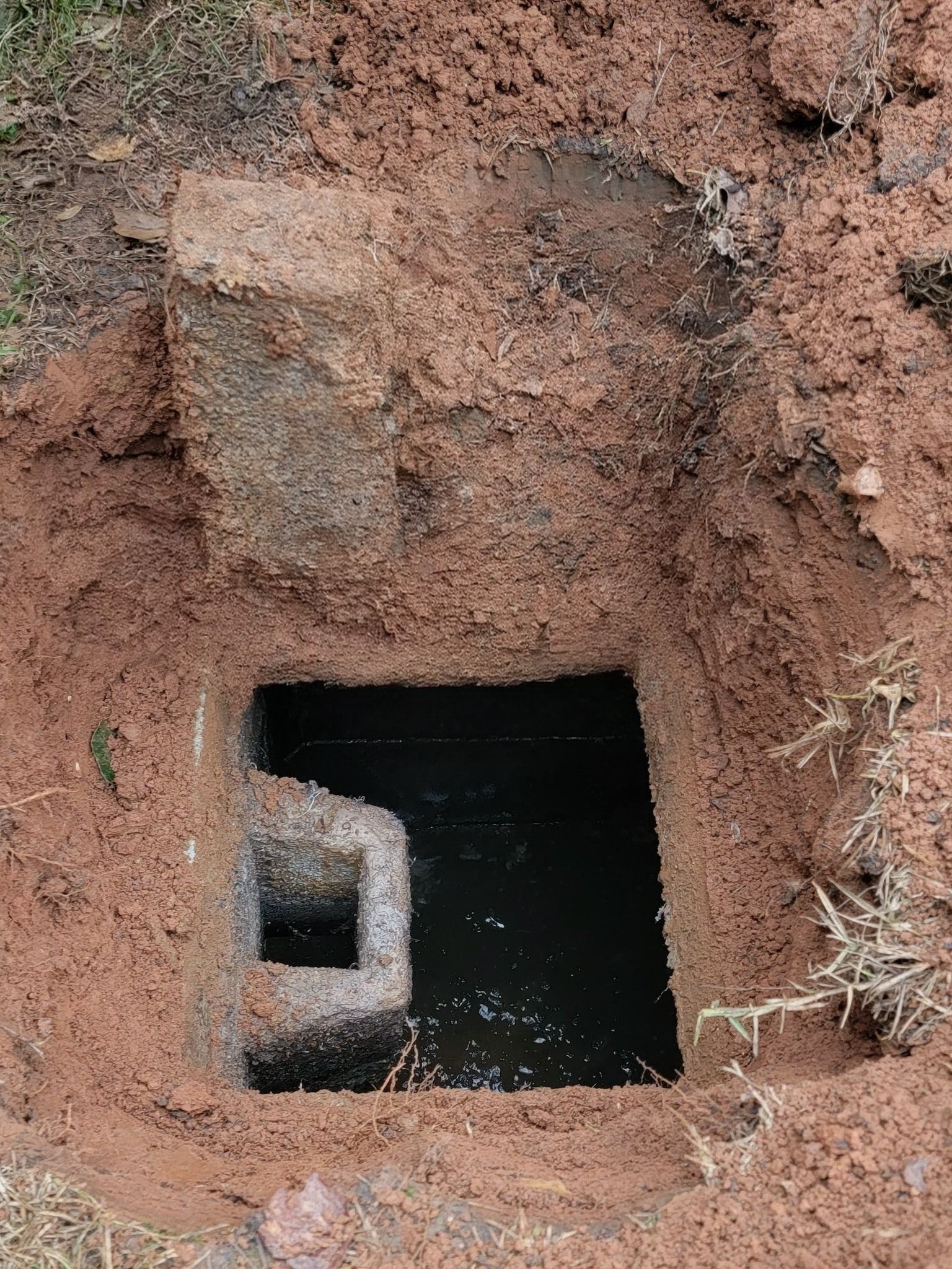 Square opening in reddish dirt wall with a dark tunnel or drain entrance inside