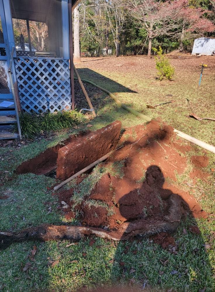 Rust-colored soil and debris piled beside a house, with a person’s shadow in the foreground.