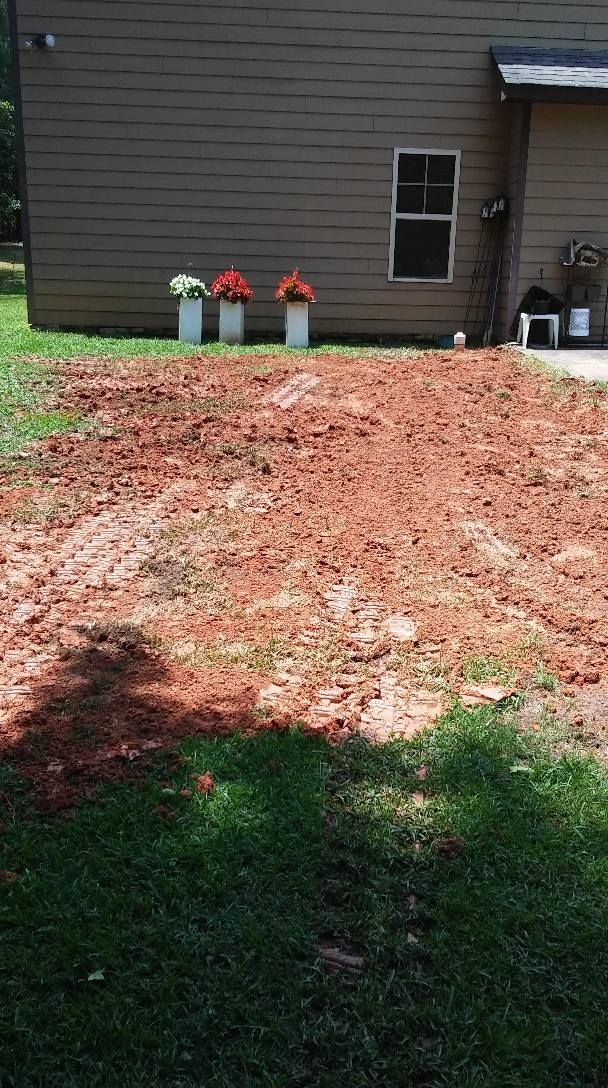 Backyard with a large bare dirt patch, grass in foreground, and house exterior with potted flowers in back