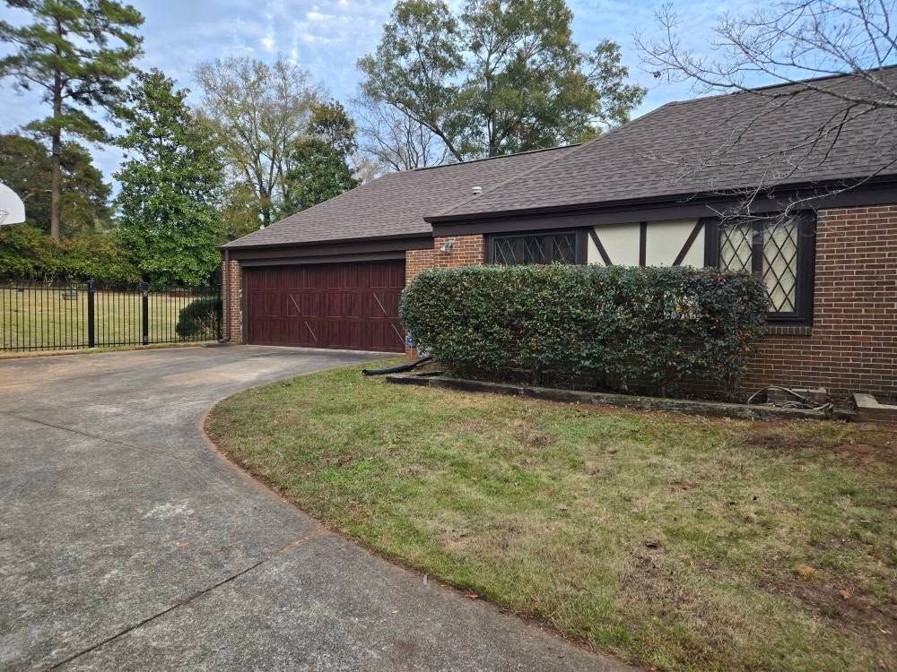 Suburban brick house with red garage and curved concrete driveway surrounded by lawn and trees