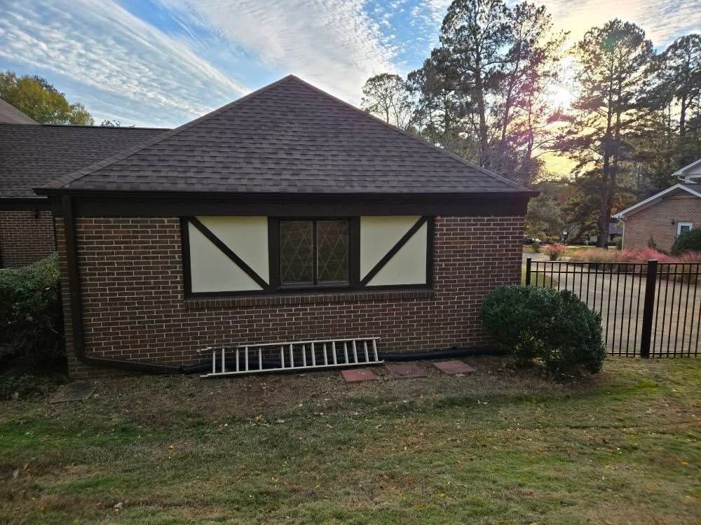 Brick house exterior with boarded windows, a ladder, and a yard at sunset