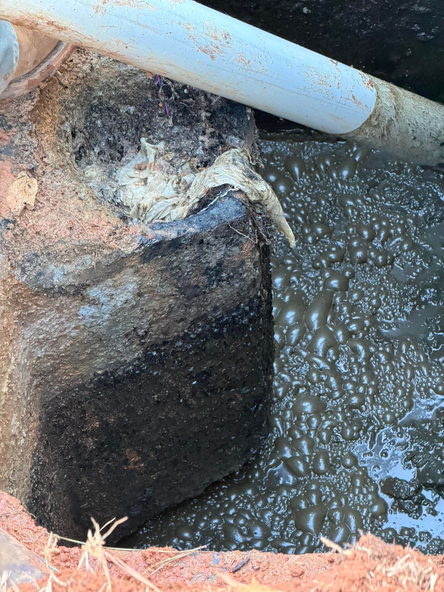 Rusty metal pipe over dark water with bubbling foam and corroded concrete edge