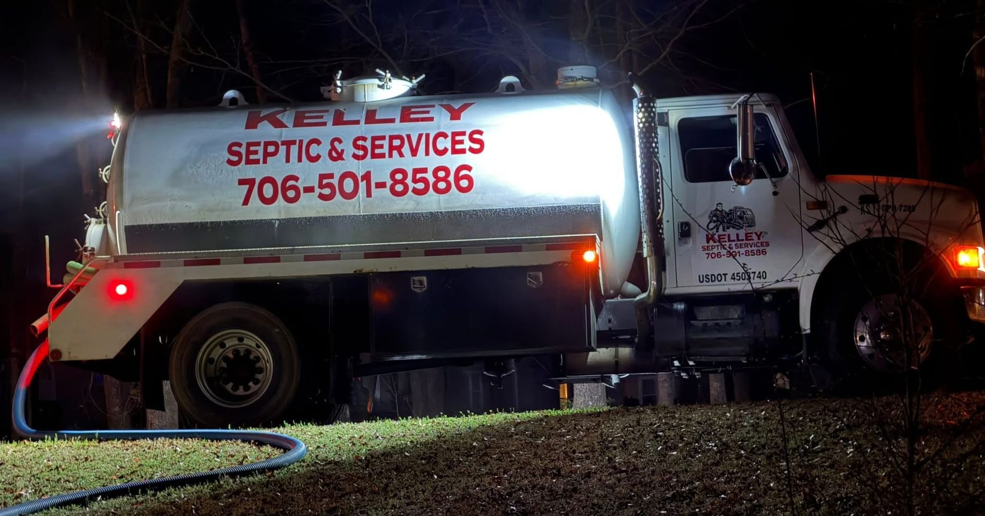 White septic service truck with red lights and hose at night, parked on a grassy roadside