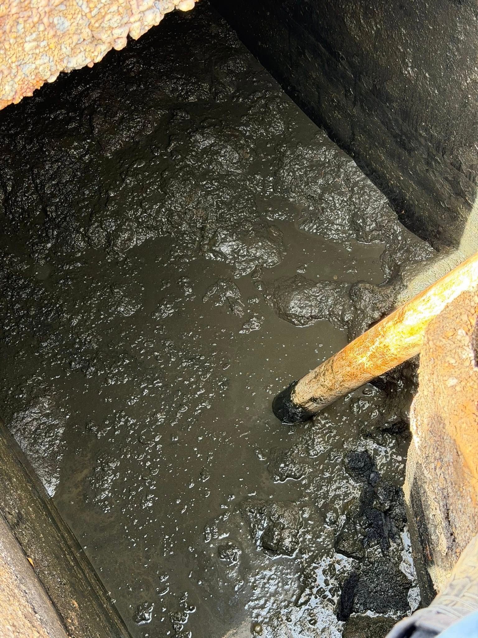 Dark muddy pit with standing water and a yellow pole or handle leaning in from the right.