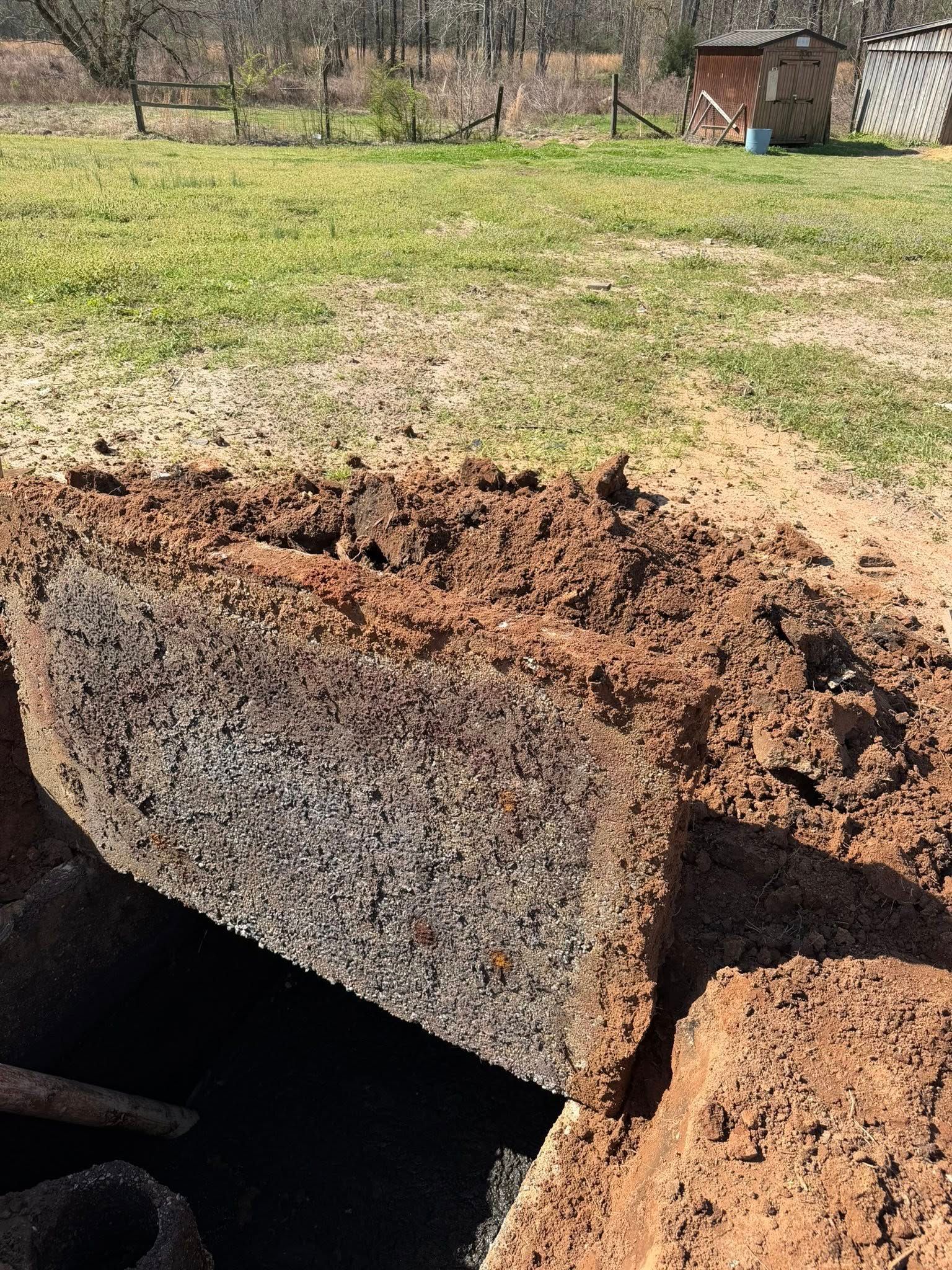 Close-up of a rusty metal culvert pipe in a grassy field with a small shed in the background.