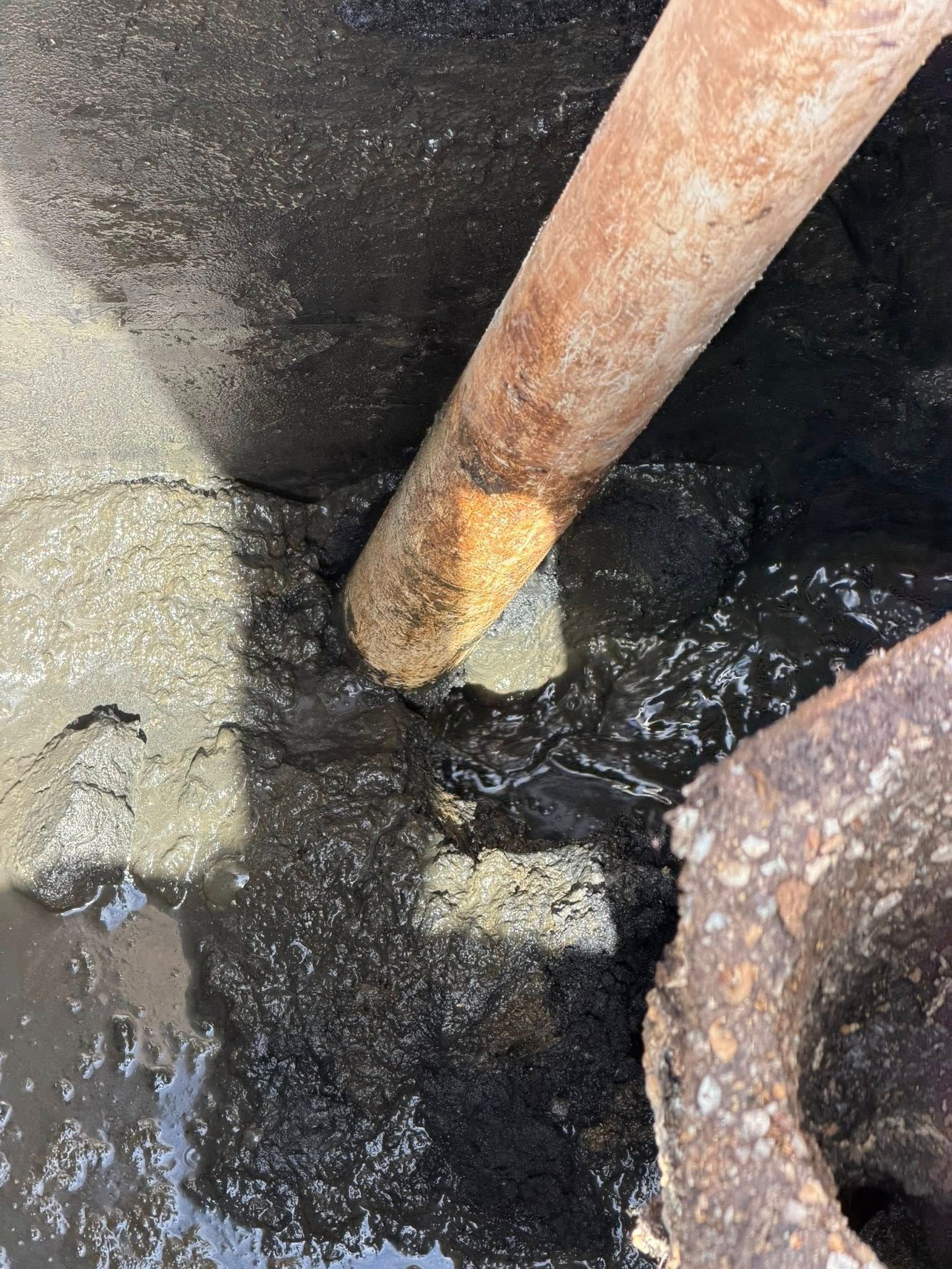Rusty pipe in black water beside a rough concrete hole.