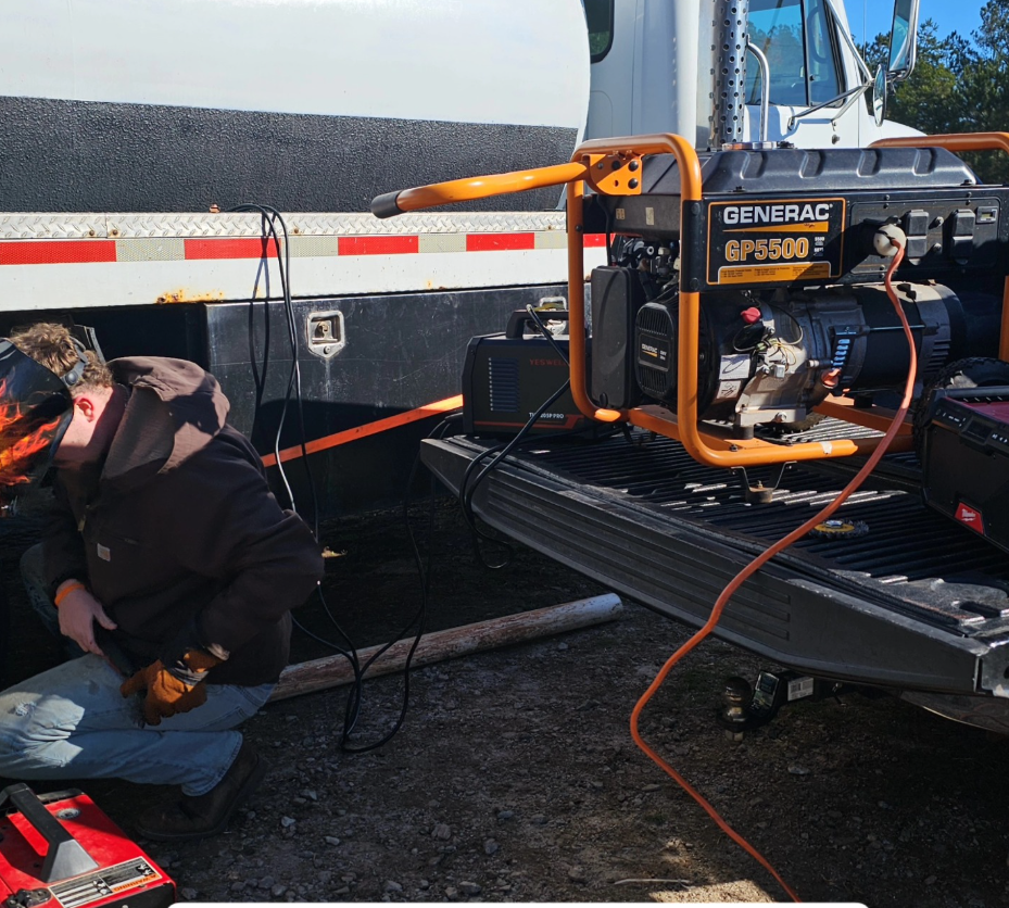 Worker kneels beside a truck bed generator with orange extension cords at a roadside work site