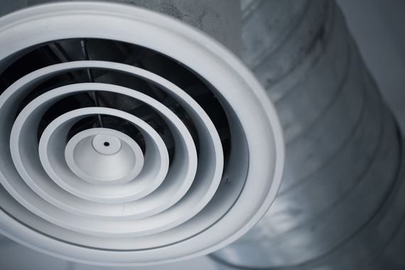 White circular air vent on a ceiling with silver ducting in the background
