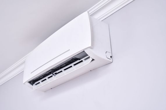 White wall-mounted air conditioner unit installed near the ceiling on a light-colored wall.