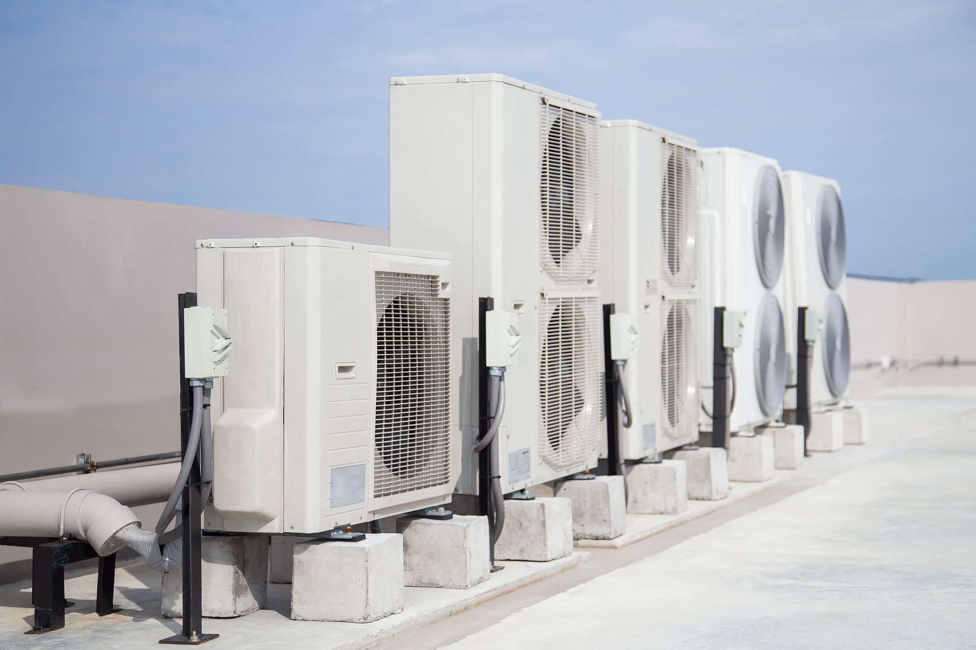 Row of rooftop HVAC units and large fans on a flat, sunlit roof