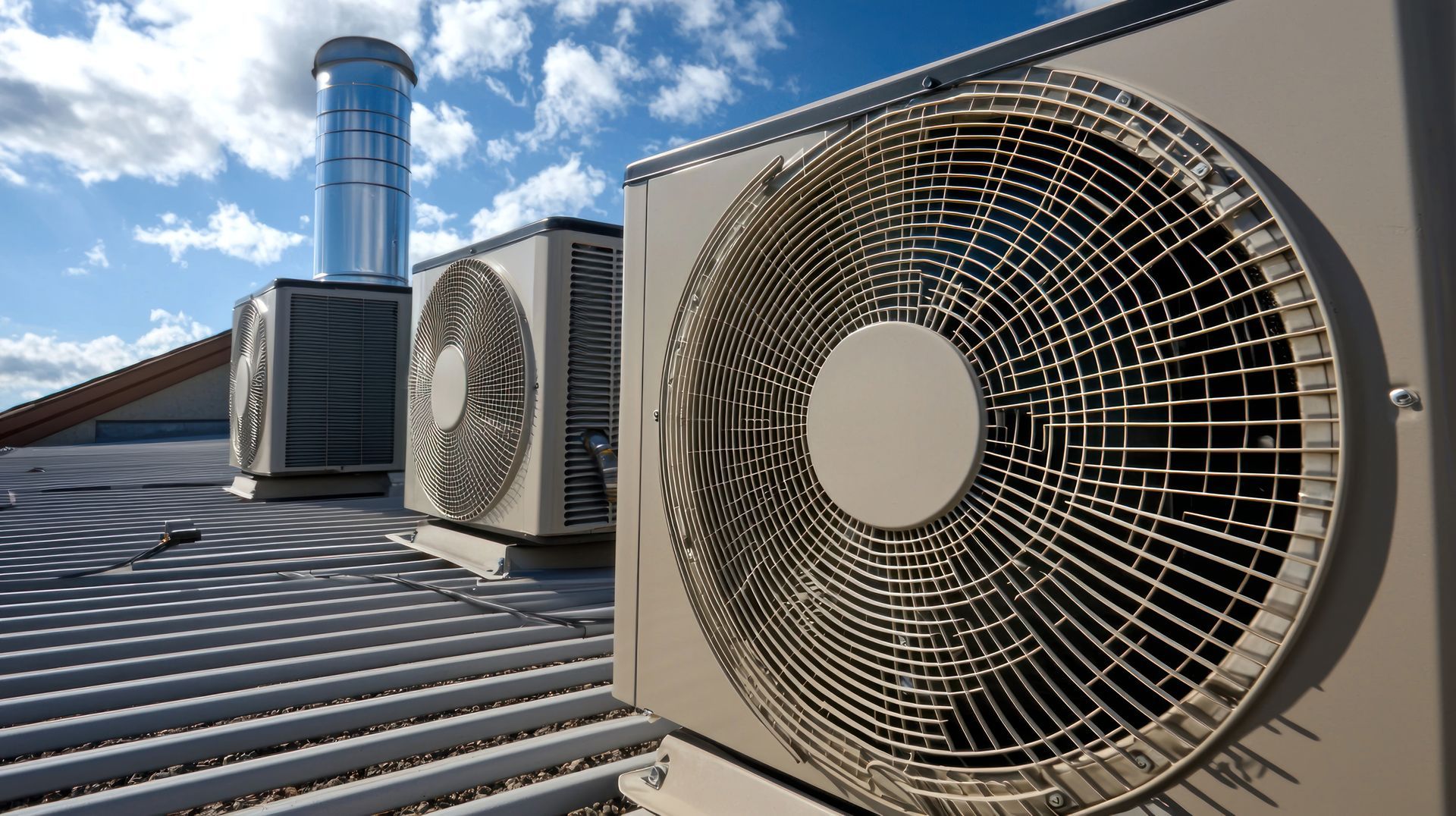 Rooftop HVAC units with large fans and a blue vent pipe under a partly cloudy sky