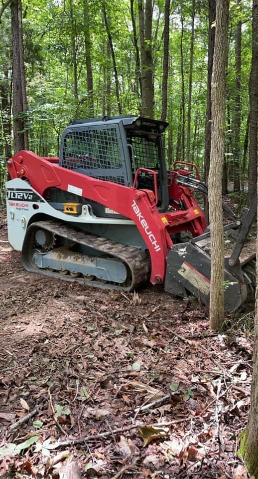 A red and white Takeuchi compact track loader sits in a wooded area covered in fallen leaves.