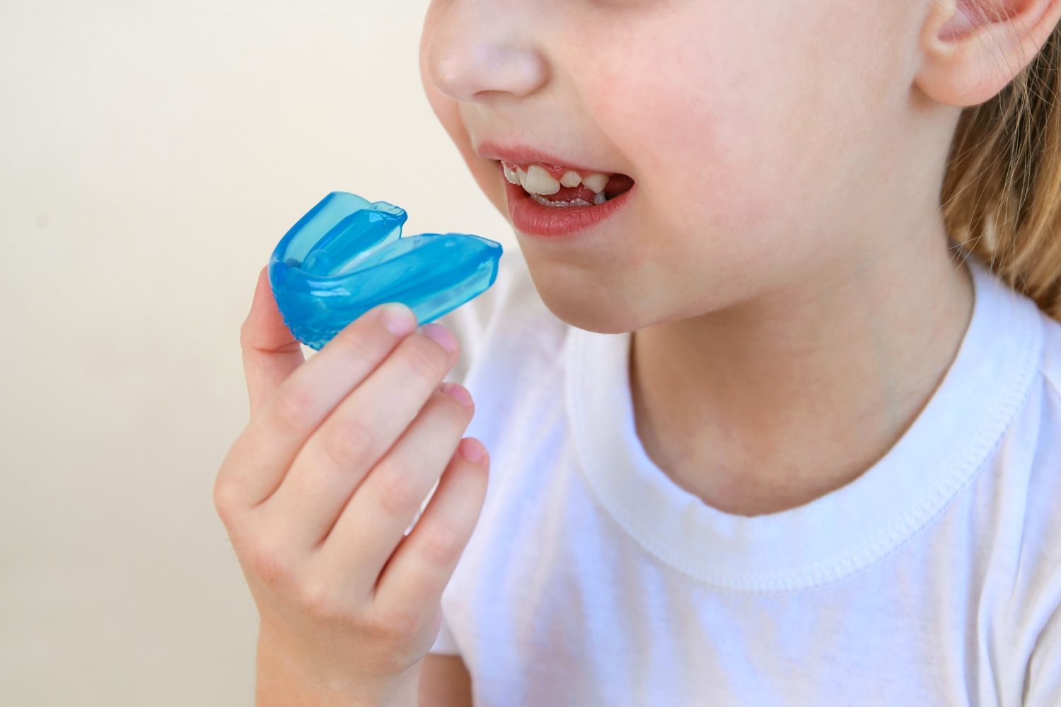 Child holding a blue dental retainer near their mouth, wearing a white shirt