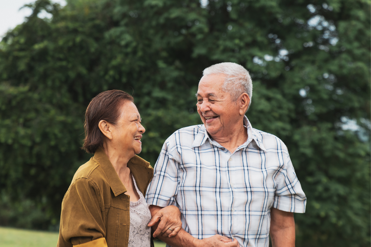 Two people smiling and chatting outdoors in front of green trees