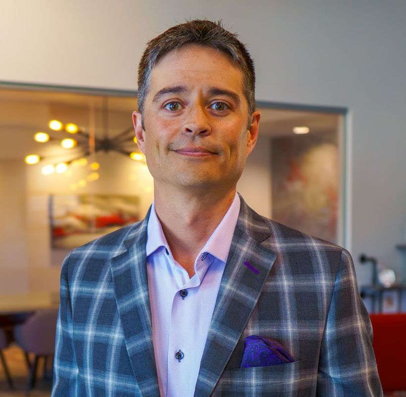 A man is wearing a plaid jacket and a purple pocket square.