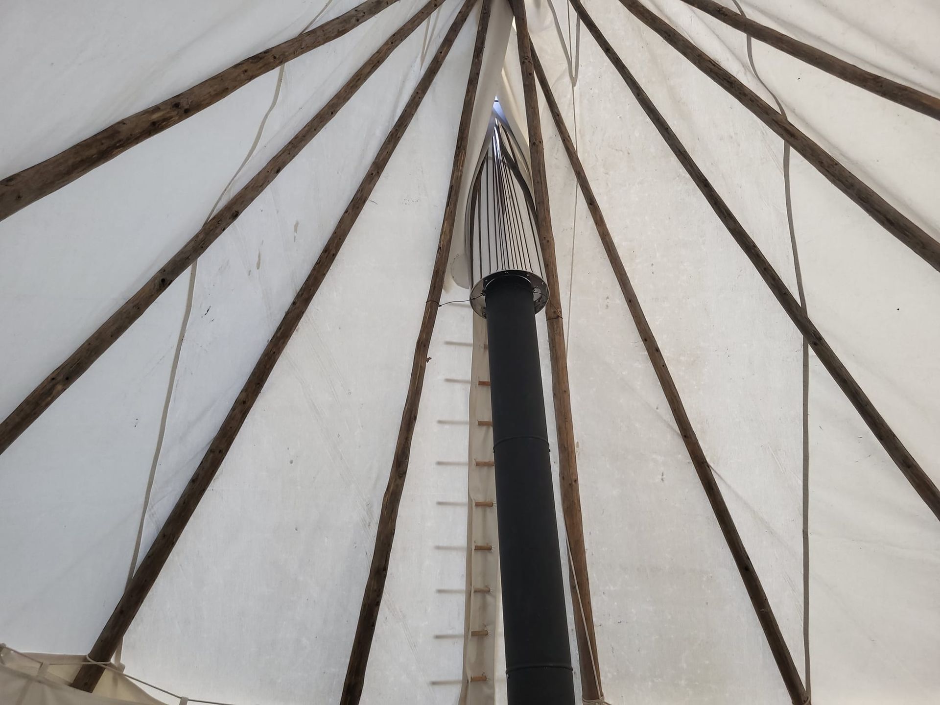 À l'intérieur d'une tente en toile blanche, montrant des poteaux en bois rayonnant à partir d'un tuyau de poêle noir central.