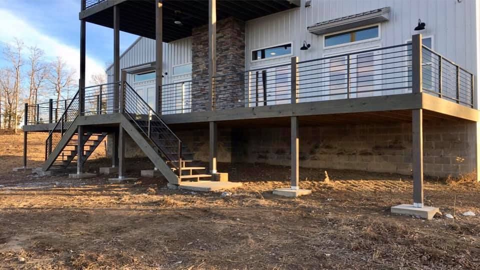 Modern two-story house with a large deck and metal railings. Staircase leads down to the yard.