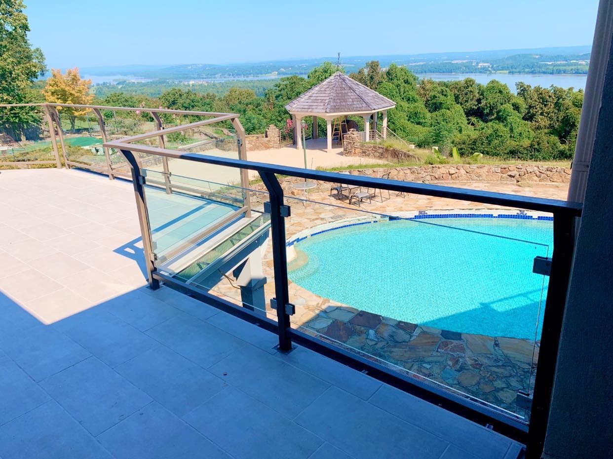 Patio overlooking a swimming pool and scenic landscape, with glass railing and gazebo in the distance.