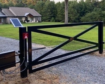 Black metal automatic driveway gate with solar panel and house in the background.